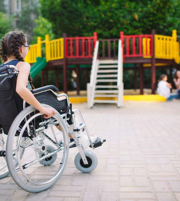 Une jeune fille en fauteuil roulant tente de rejoindre ses copines dans un parc de jeux public
